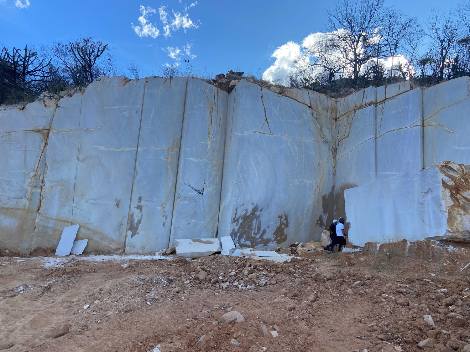 Large white stone blocks in a quarry with a blue sky and trees in the background.