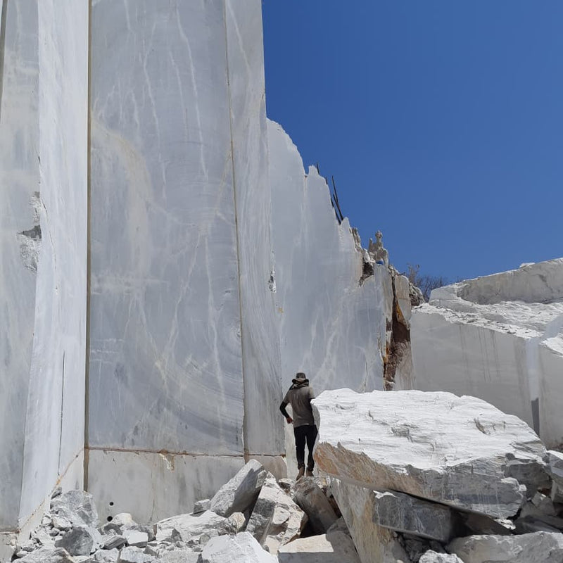 Person standing among large marble blocks in a quarry with a clear blue sky.